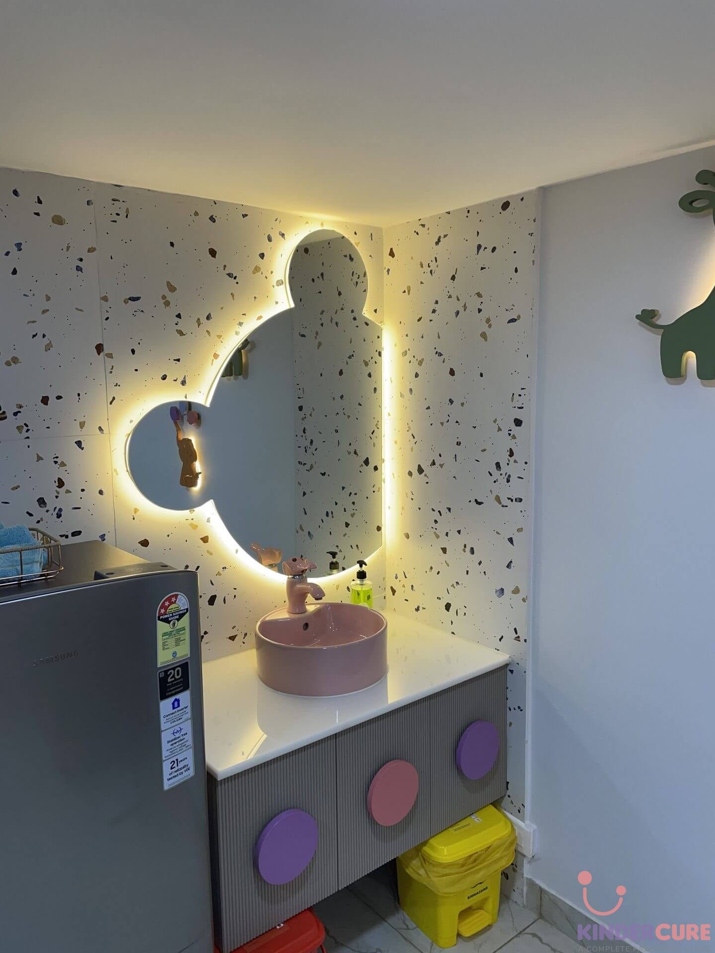 Child-friendly wash basin area with a terrazzo wall, backlit Mickey Mouse mirror, and bunny-shaped tap in KinderCure's consultation room, Gurgaon